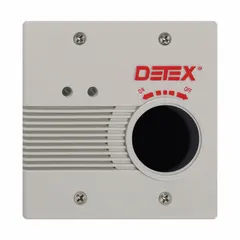 This standard door alarm features a gray plastic body and a mortise cylinder. It is powered by an electrically corded 24 V AC connection and emits a horn sound. Commonly installed on emergency exit doors to deter unauthorized use while allowing safe egress.