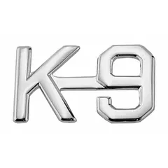 Metallic rank insignia featuring a K-9 design, constructed from metal with a silver finish. Measures 1/2 in and attaches to fabric via a clutch pin. Suitable for use on uniforms to denote K-9 unit roles.