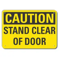 This caution sign is made of 0.055 in thick plastic with a nominal size of 7 in x 10 in. It features mounting holes for permanent indoor installation on doors or walls. The sign is not retroreflective and does not glow in the dark, suitable for posting a clear 'Stand Clear Of Door' warning in industrial facilities